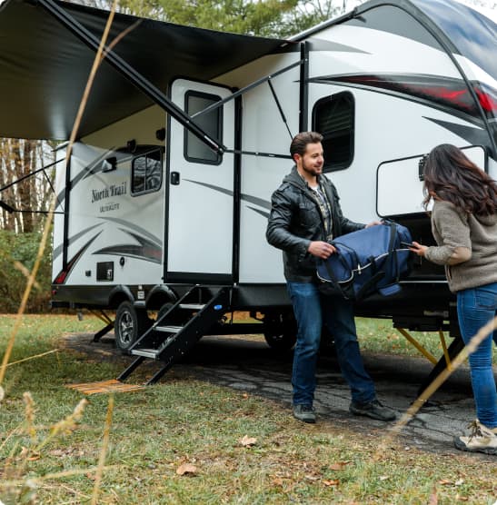 Man and woman unloading bags from a travel trailer at a campsite