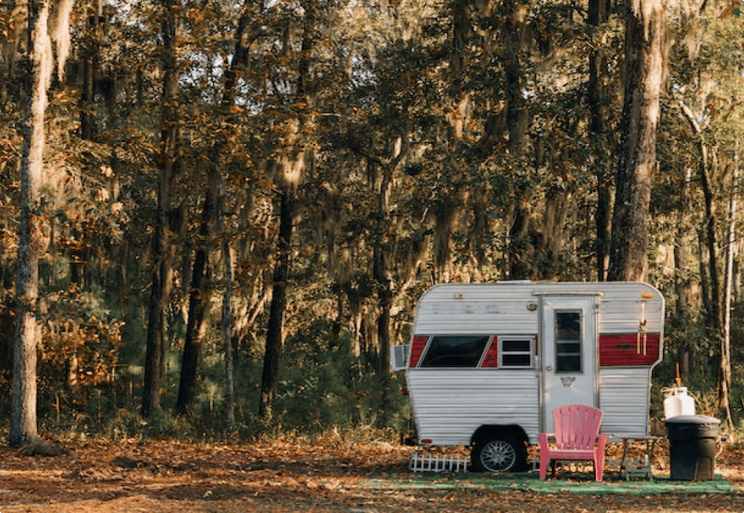 Vintage camper trailer with pink chair in wooded campsite